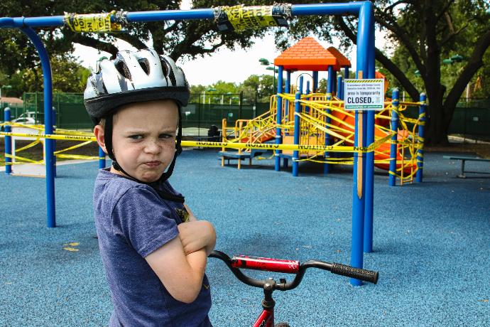 boy in blue denim vest and helmet riding red bicycle